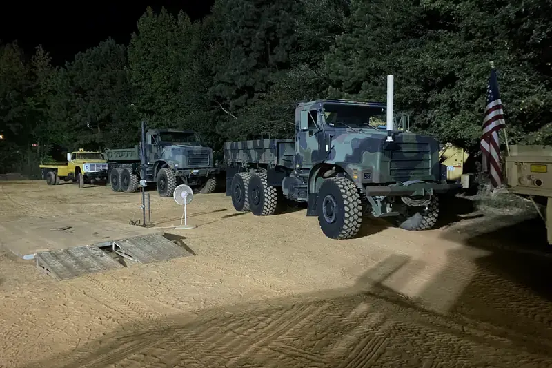 MTVR cargo and dump trucks lit up at night on a dirt lot
