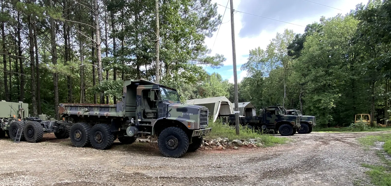 MTVR trucks lined up on a gravel lot surrounded by pine trees