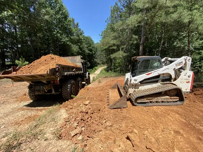 MTVR dump truck being loaded with red clay by a tracked skid steer